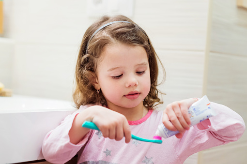 A little girl putting toothpaste on tooth brush.