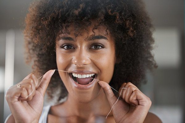 Image of a woman smiling, while flossing.